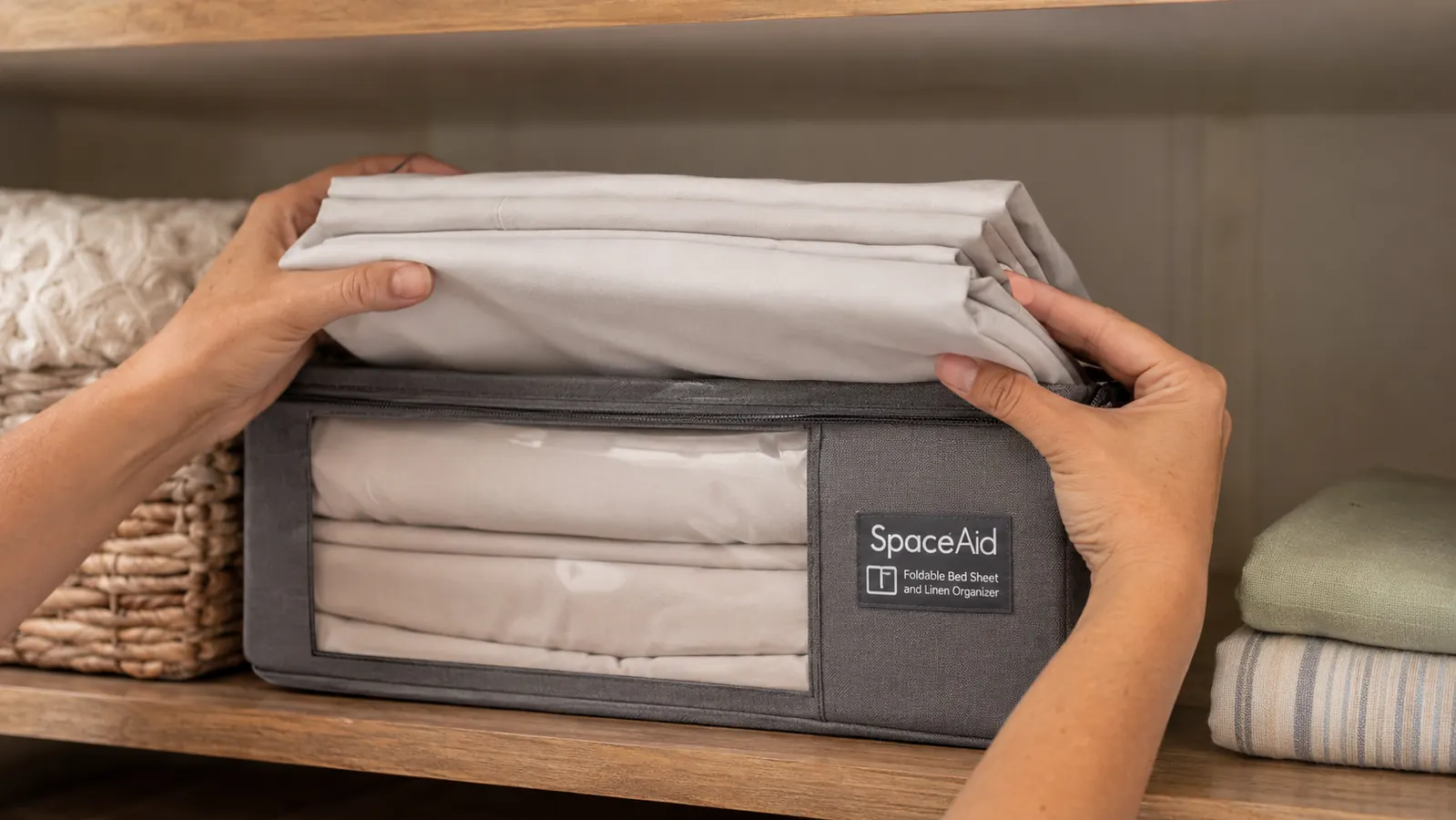 Hand tucking a folded fitted, flat, and pillowcase sheet set into a gray fabric organizer with a clear window
