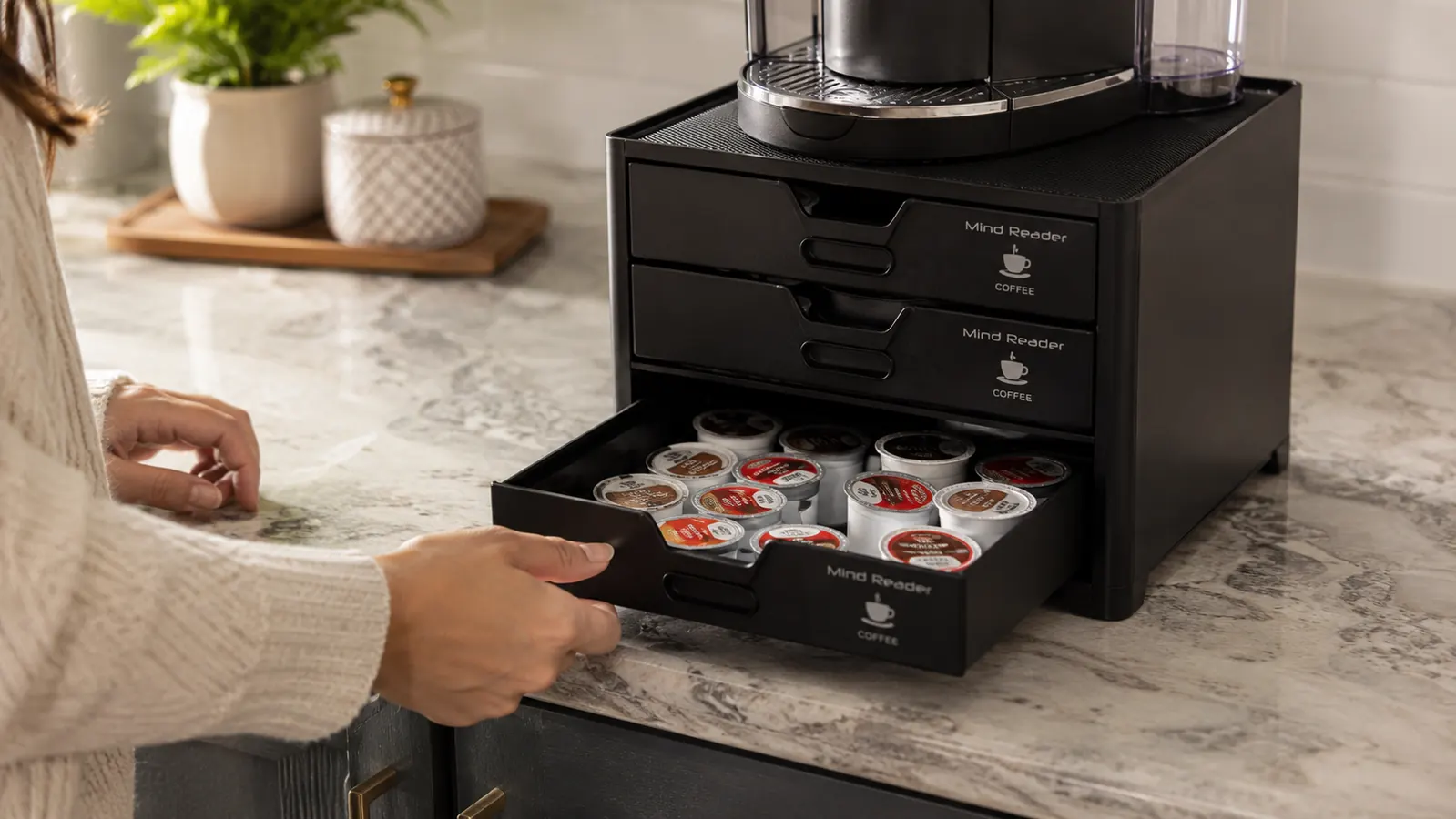 Hand pulling open a drawer of the Mind Reader coffee pod organizer to reveal rows of coffee pods sorted by roast